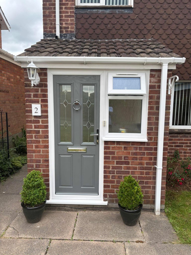 Grey composite front door and white uPVC windows on red brick house
