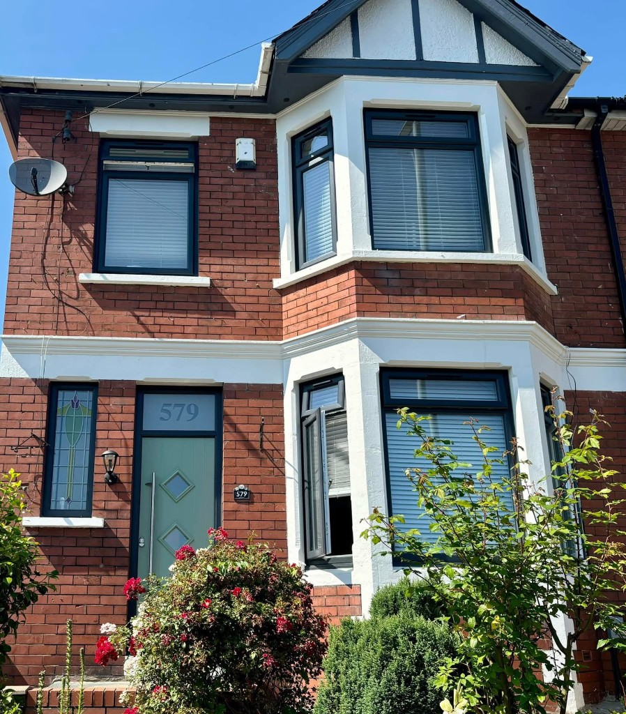 Red brick house with bay windows, dark frames and sage green front door